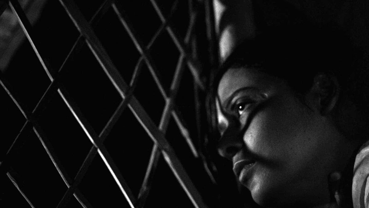 Nita, under the shadows of the window bars, her face offset in the frame